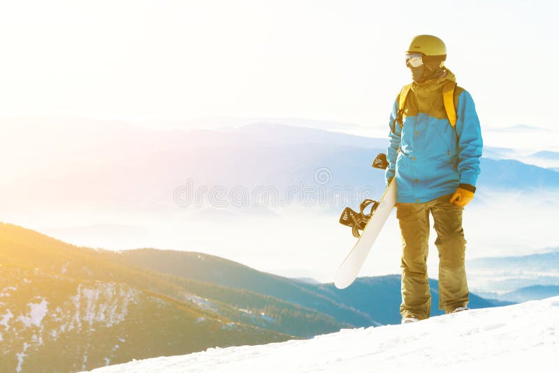 Young snowboarder with sun behind him looking at a landscape from the top of a mountain