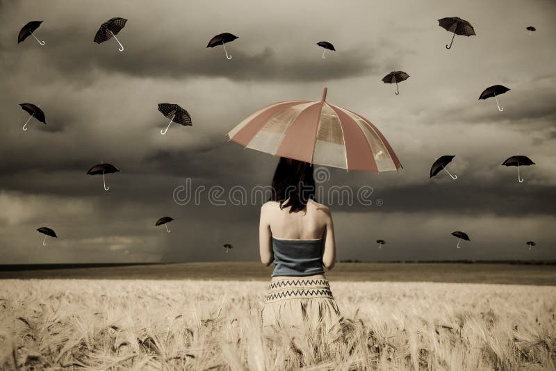 Young sorceress at wheat field with umbrella in ra
