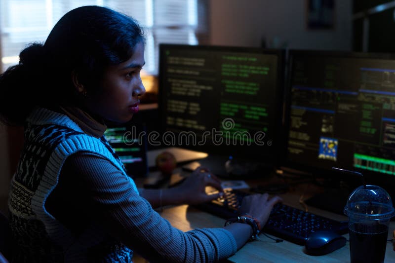 Young South Asian Woman Working on Computer Monitors in Dark Office stock photo