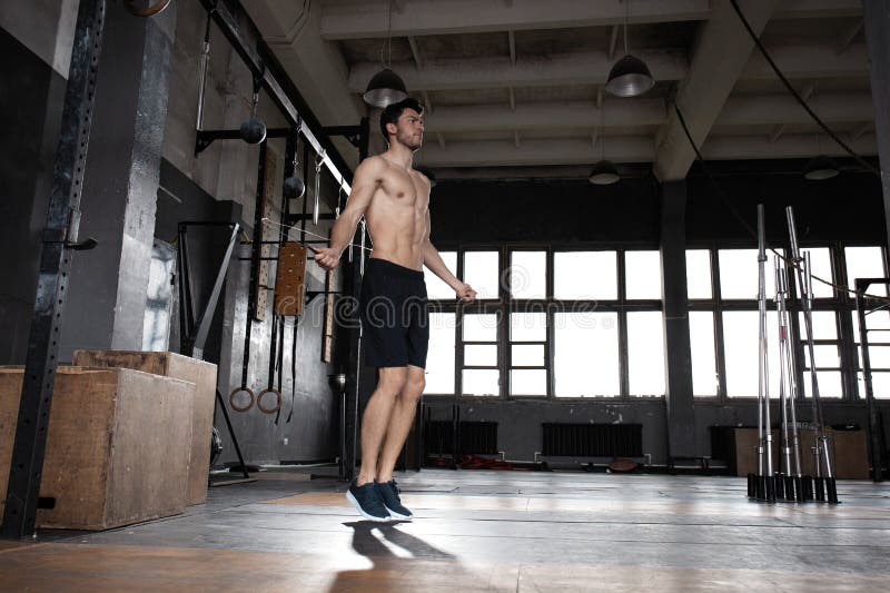 Young sportsman doing jump rope workout in gym.