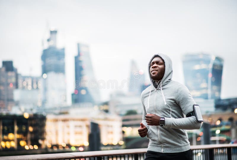 Young sporty black man runner running on the bridge outside in a city.