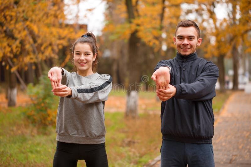 Young sporty couple doing sports in the autumn park doing an exercise on warm-up hands. royalty free stock photo Young sporty couple doing sports in the autumn park doing an exercise on warm-up hands. royalty free stock photo