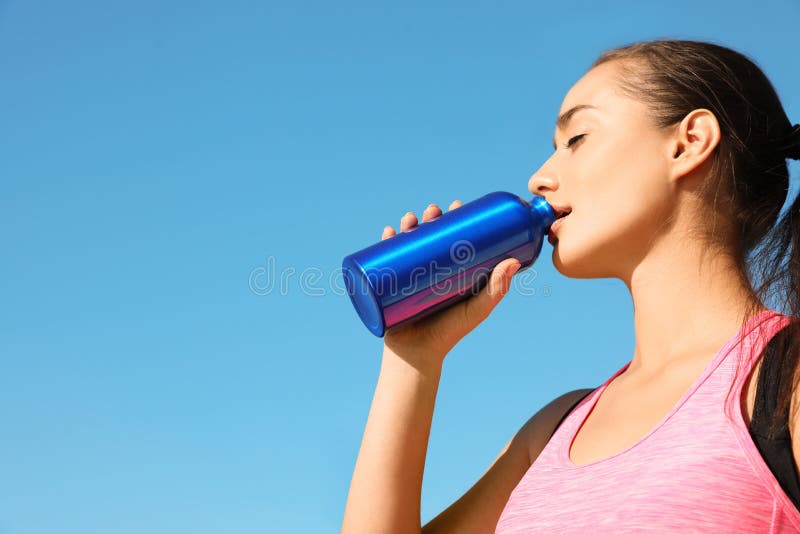 Young sporty woman drinking from water bottle outdoors on sunny day