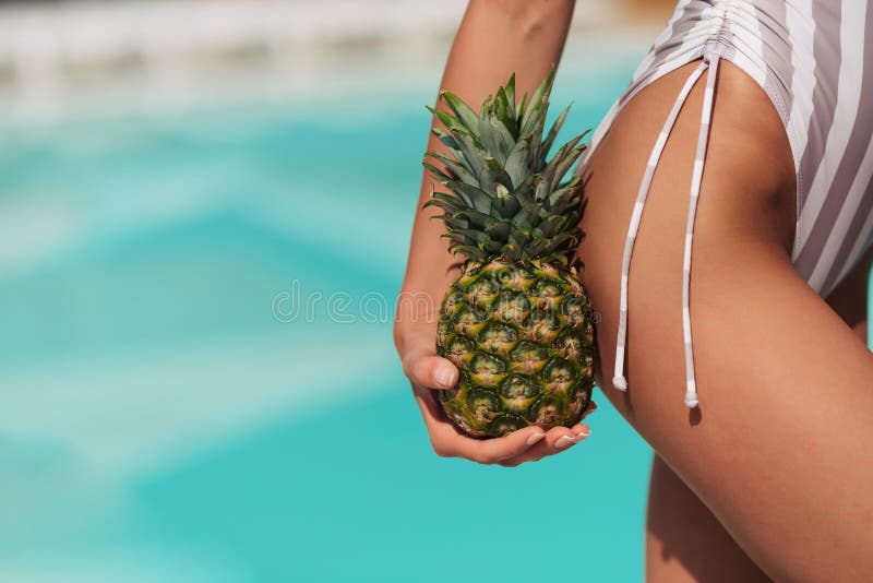 Young sporty woman in trendy sexy turquoise bodysuit hold pineapple near her perfect butt.