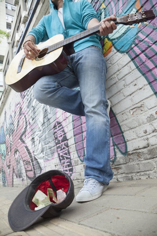 Young street musician playing guitar and busking for money in front of a wall with graffiti royalty free stock images