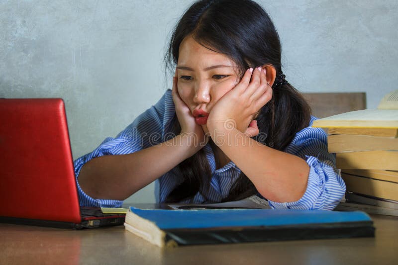 Young stressed and frustrated Asian Korean student girl working hard with laptop computer and books pile on desk overwhelmed and
