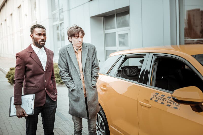 Young student wearing grey coat standing near his student driver car royalty free stock images Young student wearing grey coat standing near his student driver car royalty free stock images