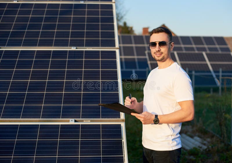 Young stylish guy in sunglasses makes an entry in folder against the background of rows solar panels stock photos