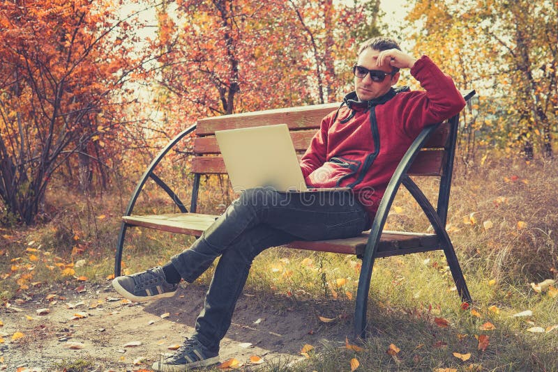 Young stylish male student texting message on laptop in park on autumn. The guy works at a laptop in the open air royalty free stock photos Young stylish male student texting message on laptop in park on autumn. The guy works at a laptop in the open air royalty free stock photos