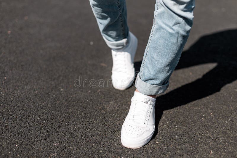 Young stylish man in leather white sneakers is walking along the road on a summer day. Male legs close-up.