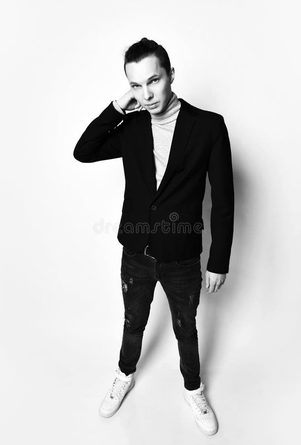 Young Stylish Man With A Modern Bun On Head In Black Jacket, Jeans And White  Sneakers Adjusts Collar Of His Grey Turtleneck Stock Image - Image Of  Laptop, Black: 146770665