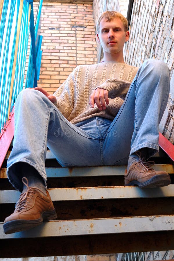 Young stylish man sit on stairs near brick wall.