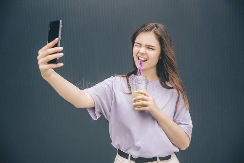 Young stylish trendy woman isolated over grey blue background. Wonderful girl taking selfie and making funny facial stock image Young stylish trendy woman isolated over grey blue background. Wonderful girl taking selfie and making funny facial stock image