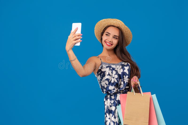 Young stylish woman posing and taking a selfie on the phone with shopping bags on a blue background