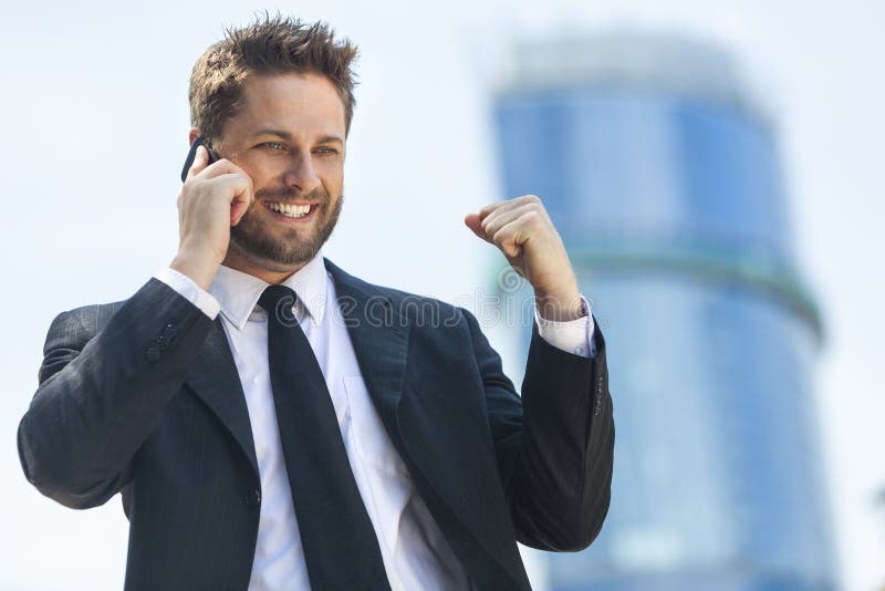 Un giovane uomo di successo, maschio esecutivo imprenditore parla di un telefono cellulare mobile celebrando a fronte di un elevato aumento di uffici in una città moderna.