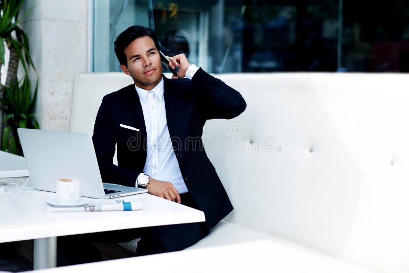 Young successful businessman in elegant suit talk on his mobile phone while sitting in modern luxury coffee shop