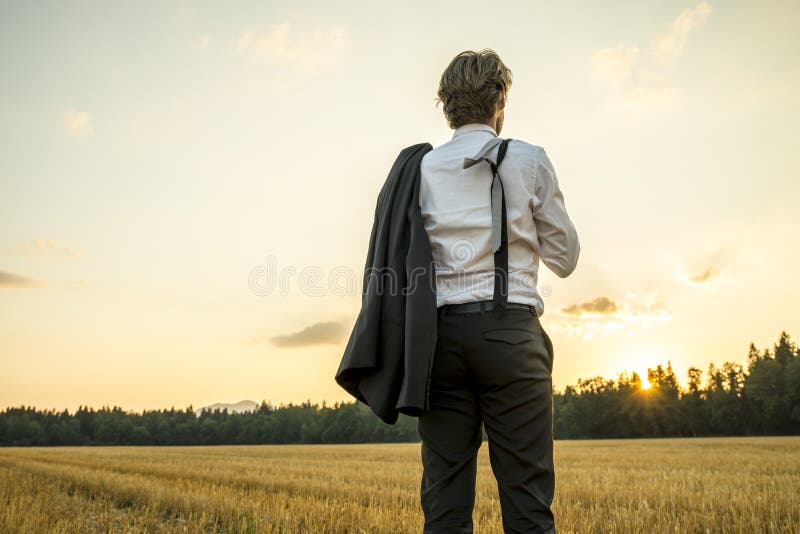 Young successful businessman standing in wheat field looking gaz