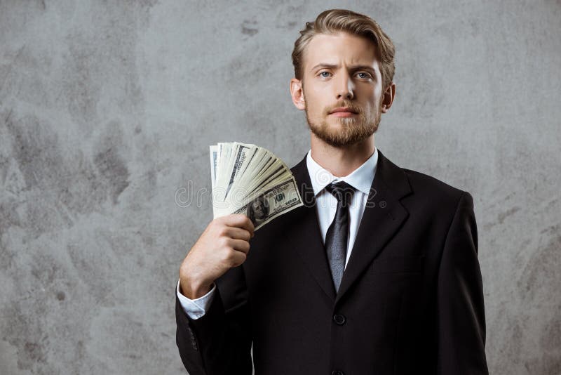 Young successful businessman in suit holding money over grey background. royalty free stock photography Young successful businessman in suit holding money over grey background. royalty free stock photography