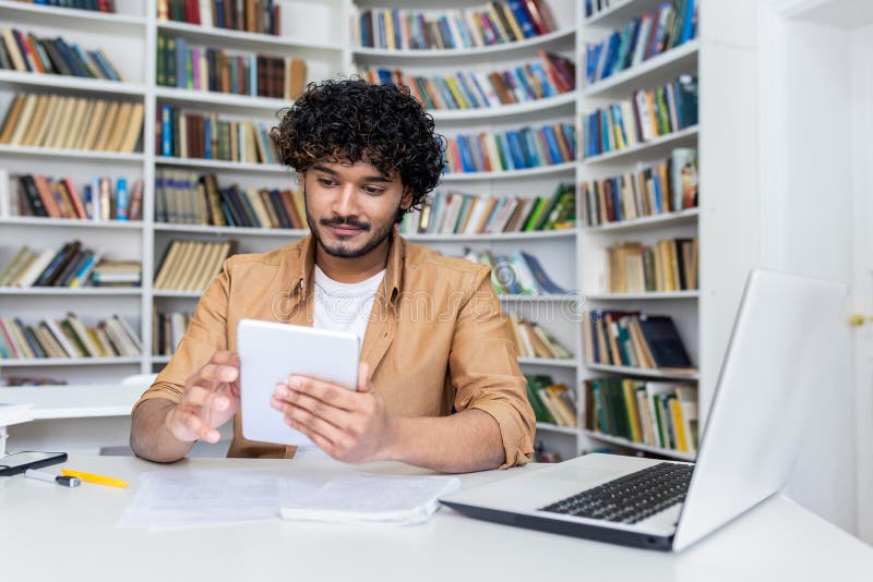 Young successful student studying sitting inside university academic library, man smiling holding tablet computer stock photos