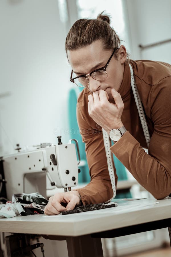 Young tall dressmaker in eyeglasses thinking about fabric for a new dress