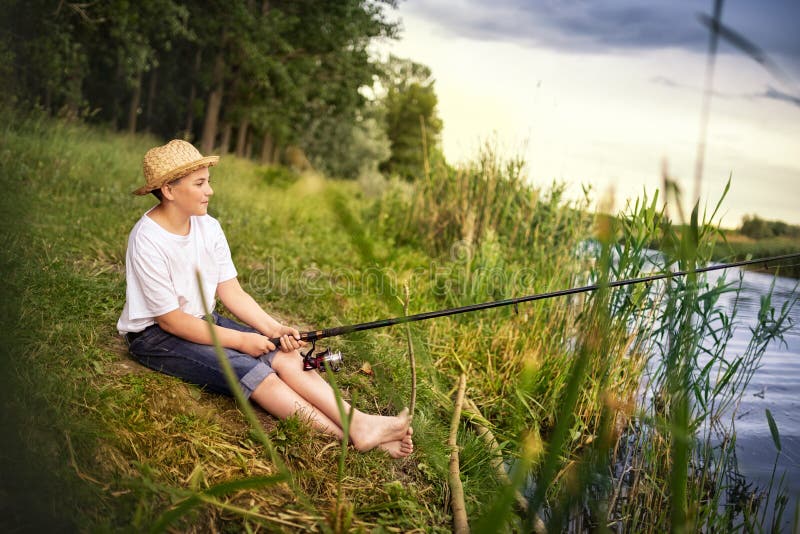 Young Teen Boy Holding Fishing Rod and Looking in River Stock