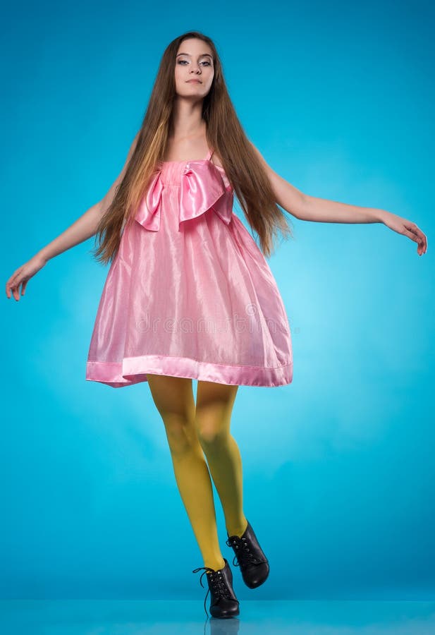 Young teen girl in a pink dress dancing in studio over blue background