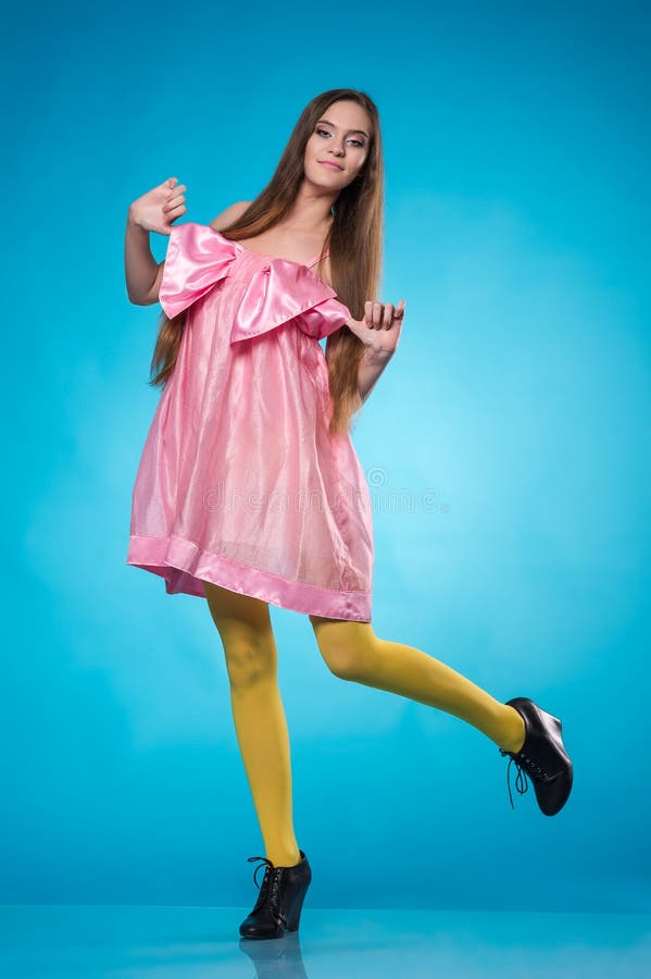 Young teen girl in a pink dress dancing in studio over blue background