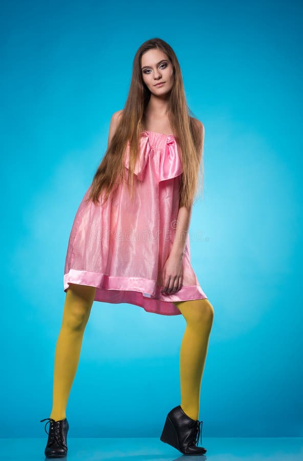 Young teen girl in a pink dress posing in studio over blue background