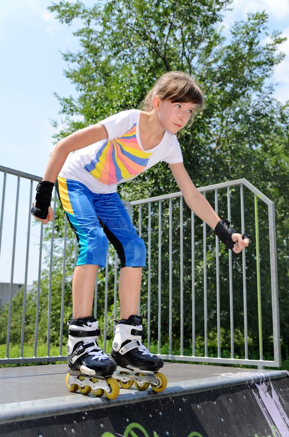 Young teenage girl roller skating balancing in her rollerblades at the top of a cement ramp in a skate park psyching herself to jump