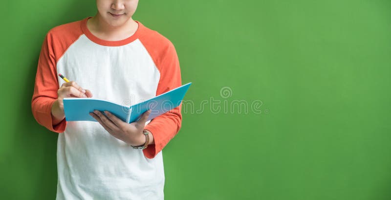 Young teenager boy writing on blue notebook leaning at green wall in school campus,Leave copy space for adding content of design