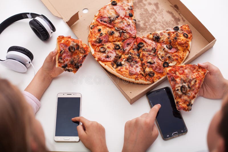 Young teenagers checking their phones while eating pizza stock images Young teenagers checking their phones while eating pizza stock images