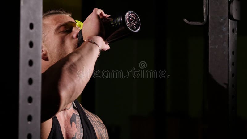 Young tired bodybuilder in a gym drinking from a shaker. 60 to 24fps 4K