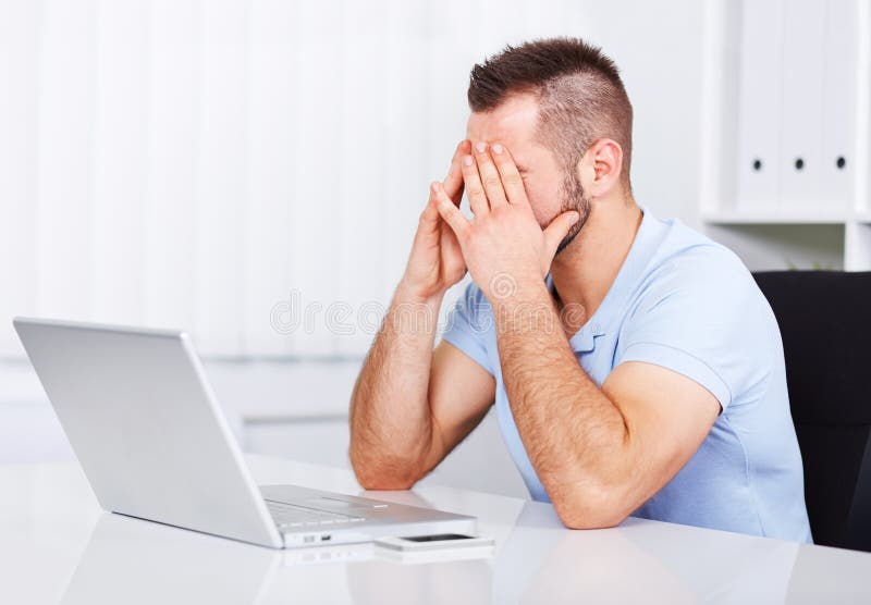 Young tired businessman rubbing his eyes in office