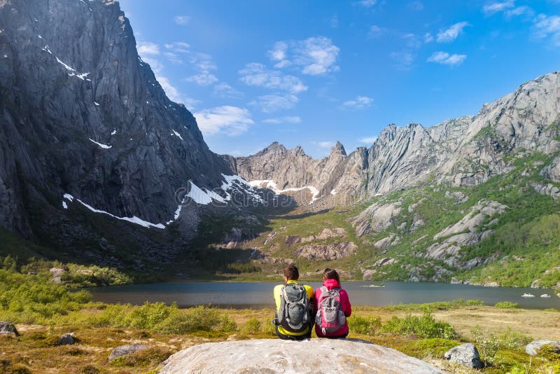 Young tourist couple sitting on stone near. Mountain lake Kallevatnet and looking at beautiful landscape stock image Young tourist couple sitting on stone near. Mountain lake Kallevatnet and looking at beautiful landscape stock image