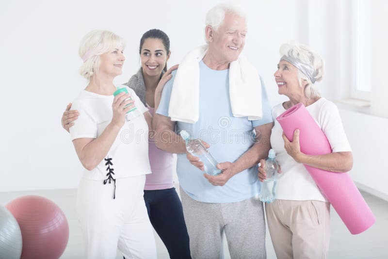 Elderly friends after physical activities. Young trainer and elderly friends in sportswear smiling after physical activities at gym royalty free stock photo