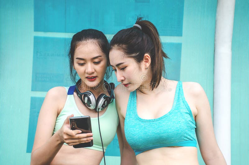 Young Two Sports Women Friends in Sports Clothes are Sitting on