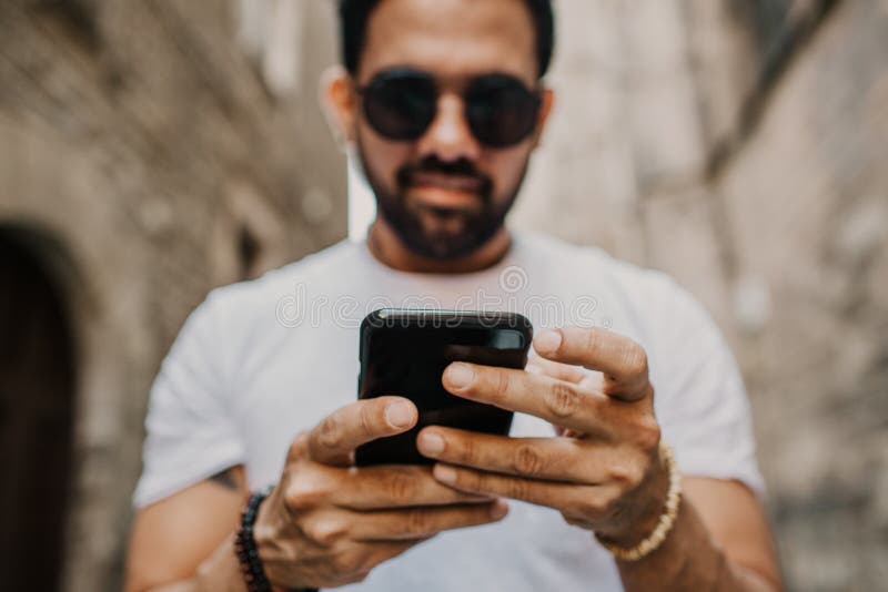 Young urban professional man using smart phone. Hipster coworker holding mobile smartphone using app texting sms message wearing sunglasses.