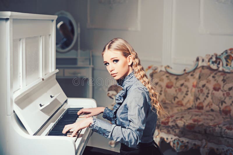 Young Victorian lady in a tender blue dress playing piano. Lovely blond woman sitting in room with vintage furniture. Home education concept.