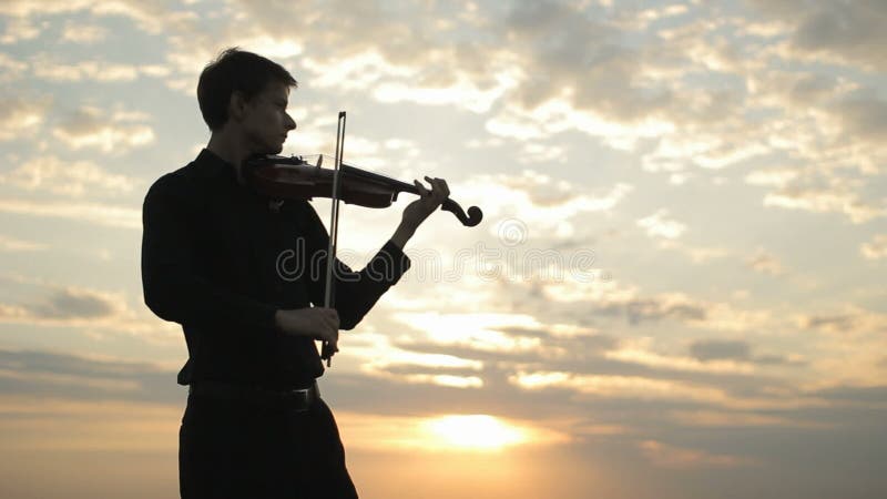 A young violinist in a black shirt, playing on the roof.