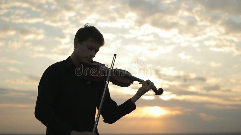 A young violinist in a black shirt, playing on the roof.