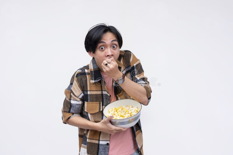 A young wide-eyed asian man voraciously stuffing his mouth with popcorn while watching a movie. Isolated on a white background royalty free stock images