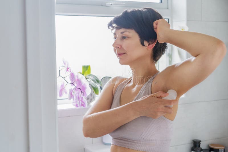 Young woman applying natural crystal alum deodorant in light modern bathroom. Eco friendly natural beauty and hygiene stock photography