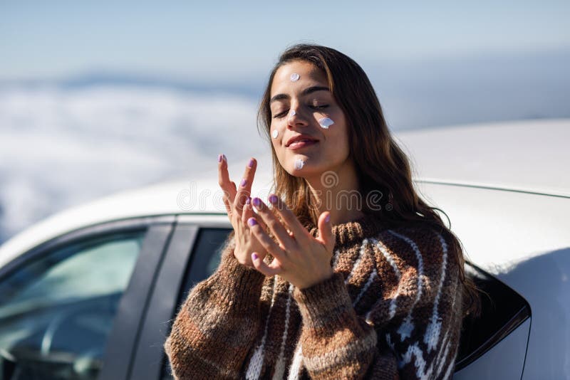 Young woman applying sunscreen on her face in snow landscape