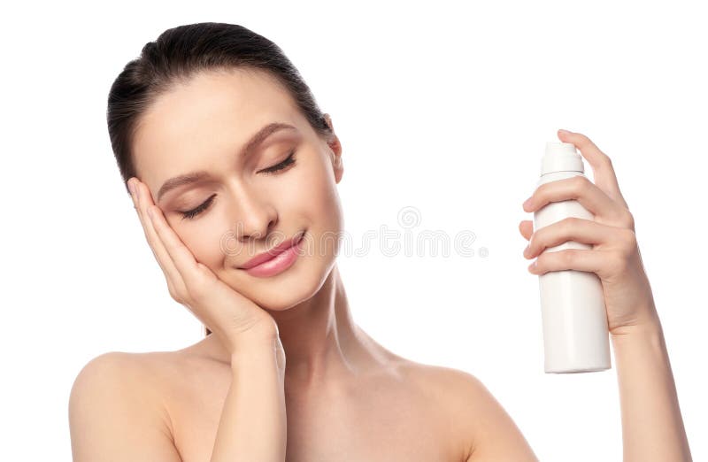 Young woman applying thermal water on face against white background