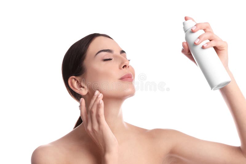 Young woman applying thermal water on face against white background