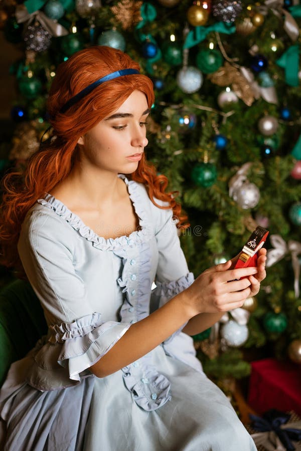 Young woman on the background of a Christmas tree with a toy in her hands in a beautiful vintage blue dress