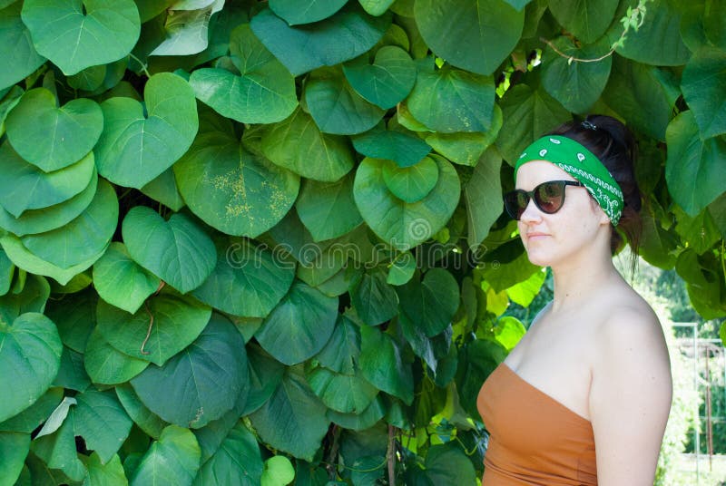 Young woman on a background of a summer green park, green leaves. A girl with black hair, a green bandage on his head, in a brown stock image Young woman on a background of a summer green park, green leaves. A girl with black hair, a green bandage on his head, in a brown stock image