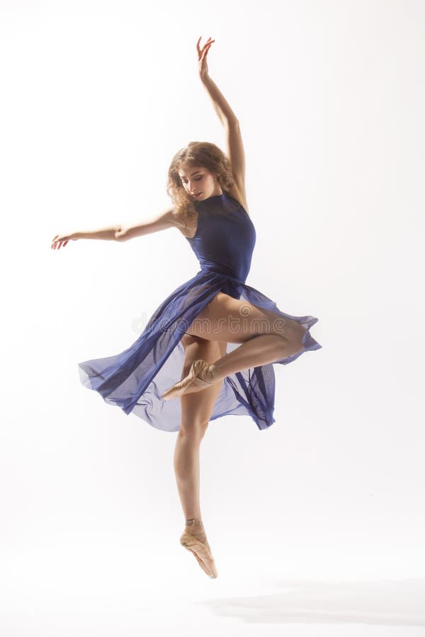 Young woman ballet dancer in pointe shoes, blue leotard and skirt, dancing in the studio against a white background. Young woman ballet dancer in pointe shoes, blue leotard and skirt, dancing in the studio against a white background