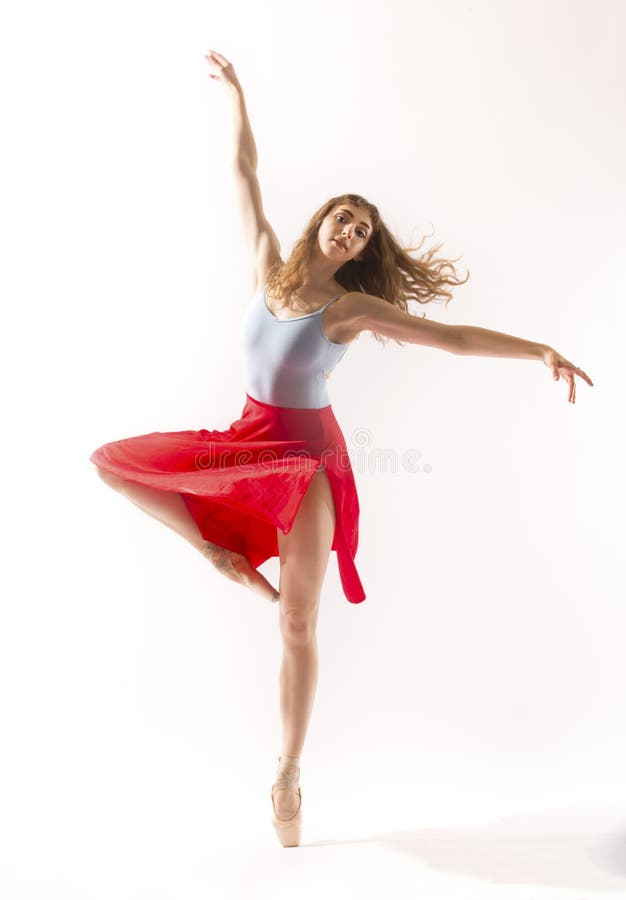 Young woman ballet dancer in pointe shoes and light blue leotard with a red skirt, dancing in the studio against a white background. Young woman ballet dancer in pointe shoes and light blue leotard with a red skirt, dancing in the studio against a white background