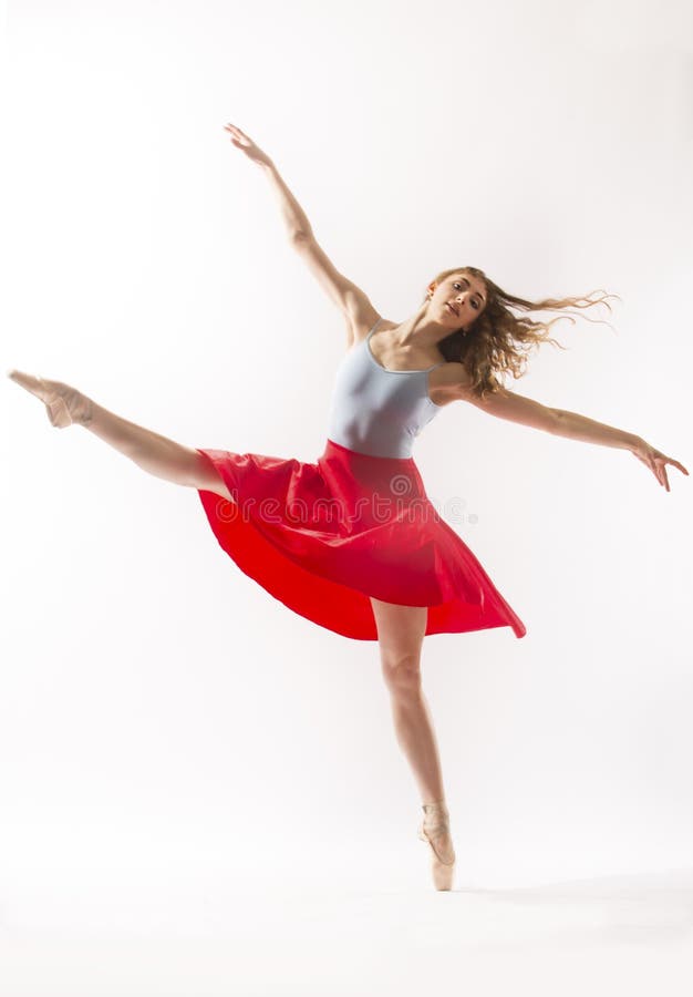 Young woman ballet dancer in pointe shoes and light blue leotard with a red skirt, dancing in the studio against a white background. Young woman ballet dancer in pointe shoes and light blue leotard with a red skirt, dancing in the studio against a white background